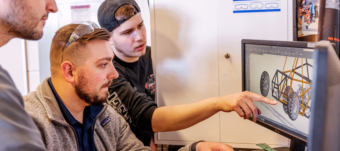 Three students pointing to a monitor